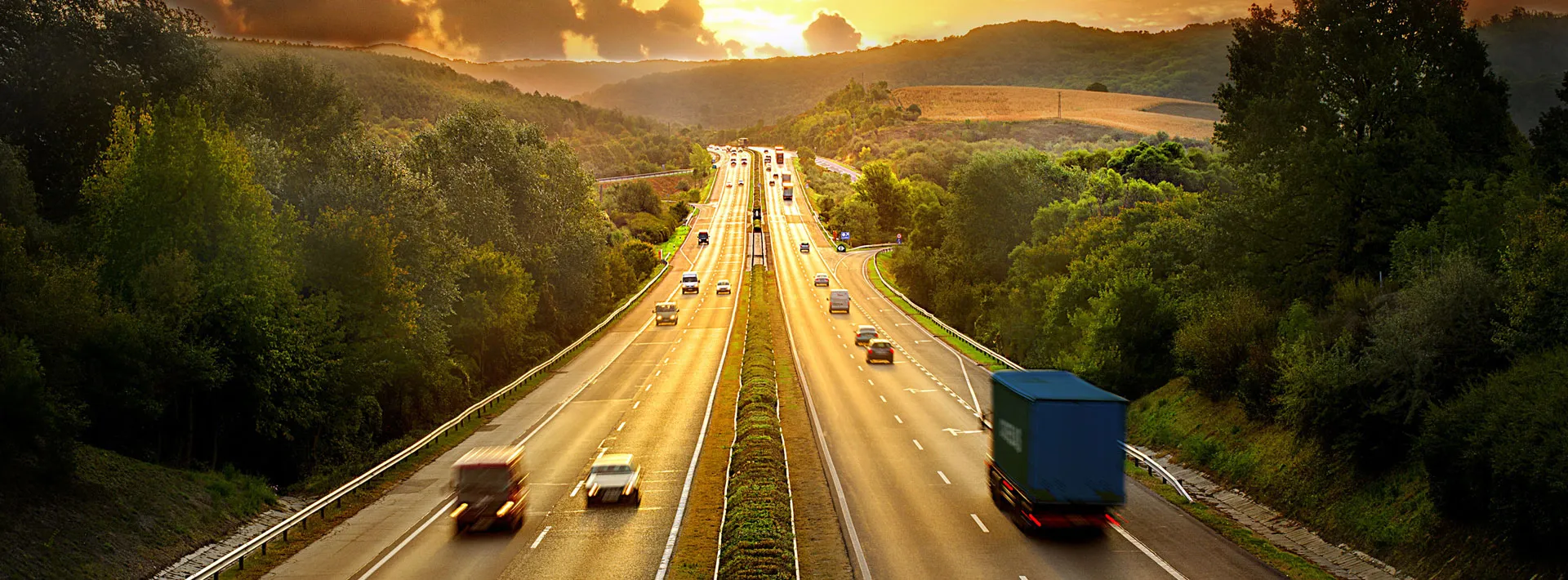 Autopista con tráfico de camiones al atardecer entre zonas boscosas